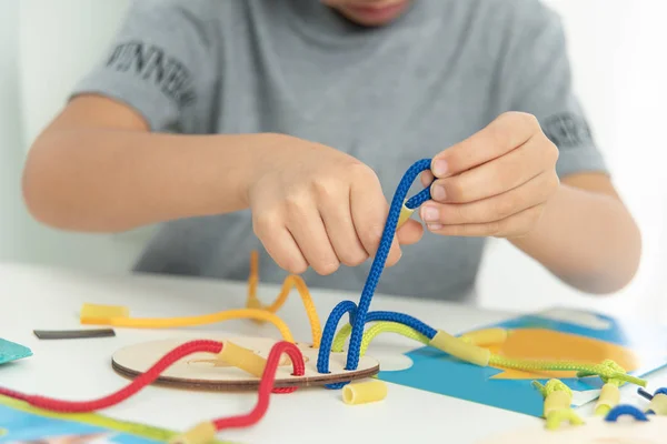 Primer plano de las manos del niño jugando con encaje o cuerda y pasta. desarrollo de habilidades motoras finas. Educación temprana, método Montessori. Habilidades cognitivas , — Foto de Stock