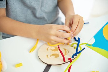 Dantel, ip ve makarna ile oynayan çocuk ellerini kapat. Kaliteli motor becerilerin gelişimi. Erken eğitim, Montessori Metodu. Bilişsel beceriler,