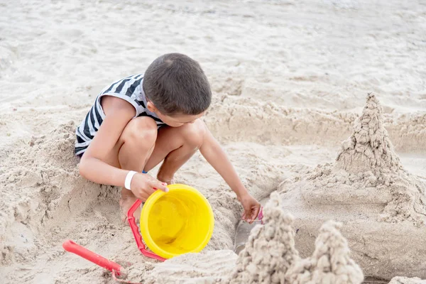 Criança constrói areia Castelo por mar. criança na praia brincando com areia . — Fotografia de Stock