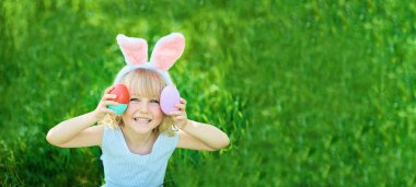 Cute funny girl in bunny ears holding eggs at garden during at Easter egg hunt,easter concept 