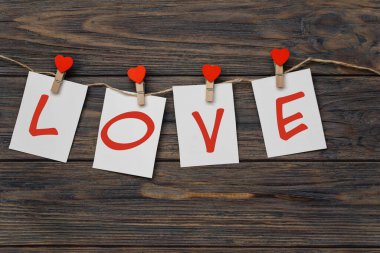 red hearts shaped clothespins with love inscription on empty paper notes hanging on rope on wooden background, Happy Valentine day concept 