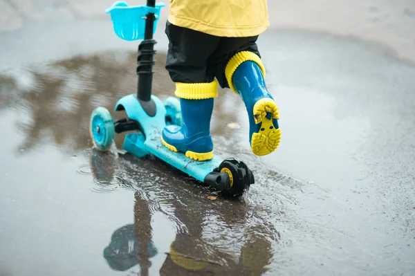 黄色のレインコートの幸せな小さな子供は 雨の後の暖かい夏の日に水たまりの向こうのスクーターに乗っています 子供のためのアクティブなレジャー 屋外で楽しんでいる子供 — ストック写真