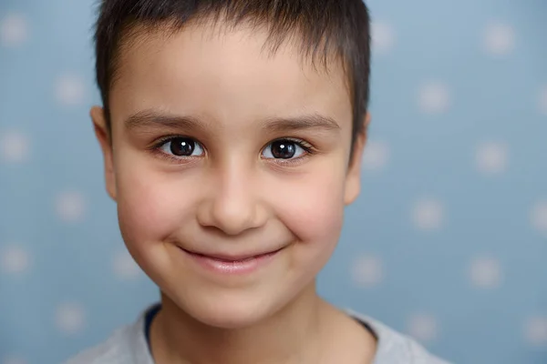 照片上英俊的小男孩笑着看着蓝色摄影棚背景的相机 — 图库照片