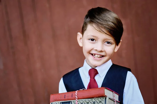 一个快乐的学童拿着红色木制背景的书站在那里的画像 知识的日子 学年开始时 — 图库照片