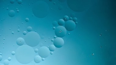 Koyu mavi arka planda köpüklü yağ. Soyut alan arkaplanı. Yumuşak seçici odaklanma. Su yüzeyine makro yağ damlaları. kopyalama alanı. Su içindeki hava kabarcıkları, yatay biçim, sosyal medya 16x9