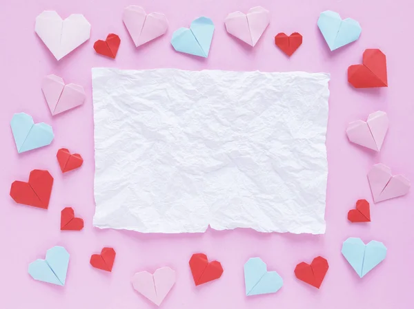 color paper origami hearts and crumpled white paper with space on pink background.