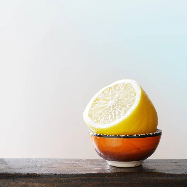 Lemon slice in orange ceramic bowl on wooden surface on light blue background.