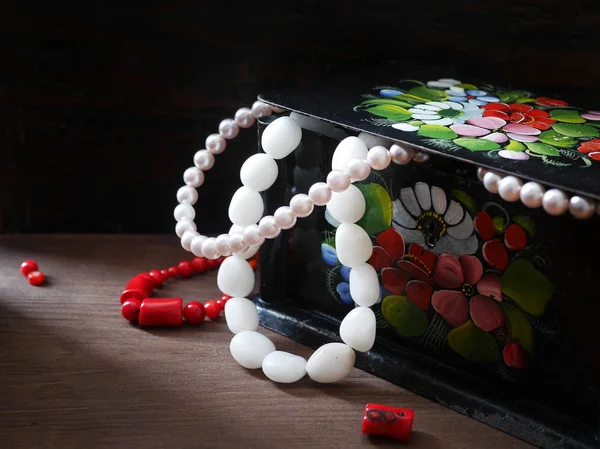Jewelry in an old lacquered painted black box, a string of pearls and beads from white agate hang from the box. Black background.