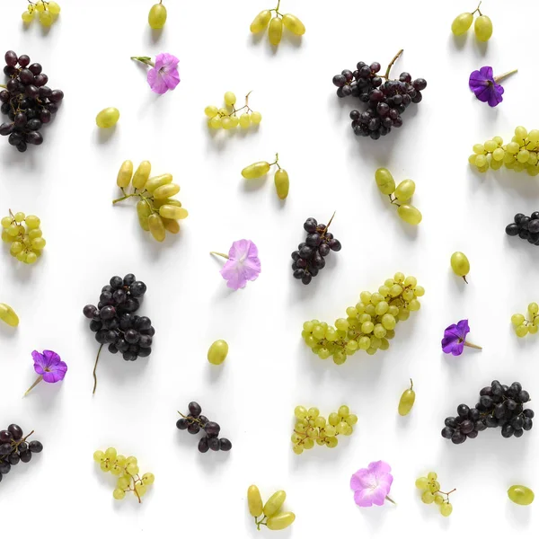 close-up photo of fresh fruits set of white and blue grapes with flowers on white table background