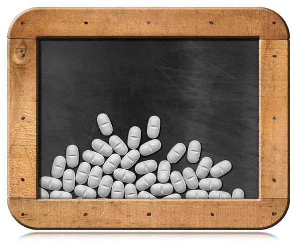 Pílulas brancas em um quadro negro com moldura de madeira — Fotografia de Stock