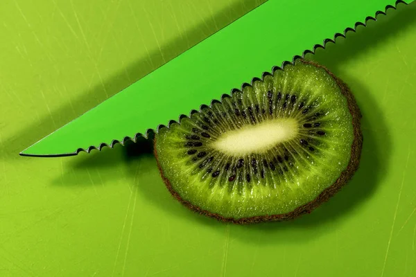 Fatia de kiwi em uma placa de corte com faca verde — Fotografia de Stock