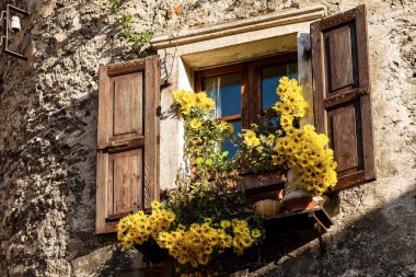 Close-up of an old window with wooden shutters and yellow flowers in the medieval village of Canale di Tenno or Villa Canale, Italian Alps, Trento province, Trentino-Alto Adige, Italy, Europe clipart