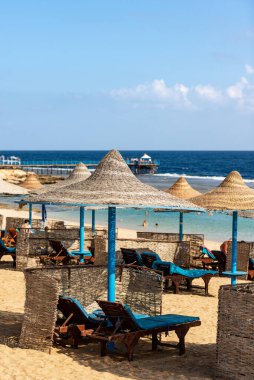 Kızıl Deniz kumlu bir plajda, Marsa Alam, Mısır, Afrika yakınlarındaki bir turizm beldesinde saman şemsiyeleri ve güverte sandalyeleri. 