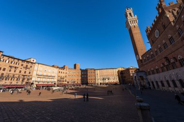 SIENA, TUSCANY, ITALY - 5 Ocak 2017: Piazza del Campo, Torre del Mangia (Eski Kule) ile Siena 'nın ana şehir meydanı. Bazı turistler ve yerliler güneşli bir kış gününde meydanda yürüyorlar..