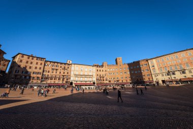 SIENA, TUSCANY, ITALY - 5 Ocak 2017: Piazza del Campo, antik ortaçağ sarayları ile Siena 'nın ana şehir meydanı. Bazı turistler ve yerliler güneşli bir kış gününde meydanda yürüyorlar..