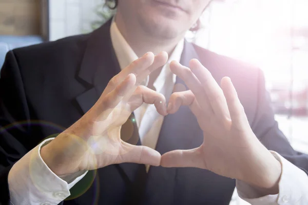Businessman in cafe shows hand heart sign