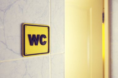 WC işareti tuvalet oda girişinde asılı siyah harflerle sarı