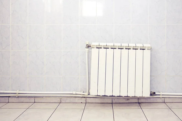 Radiatore di riscaldamento bianco su parete piastrellata con tubi in bagno pubblico — Foto Stock