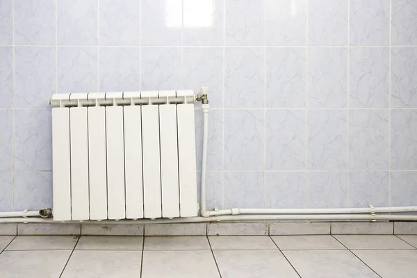 Radiatore di riscaldamento bianco su parete piastrellata con tubi in bagno pubblico — Foto Stock