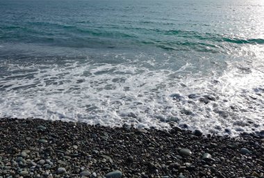 Çakıl taşlı deniz kıyısı. Sahilde ıslak deniz taşları ve sessiz deniz sörfü.