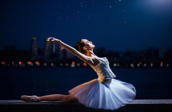 Балерина в белом платье на фоне ночного города и реки
