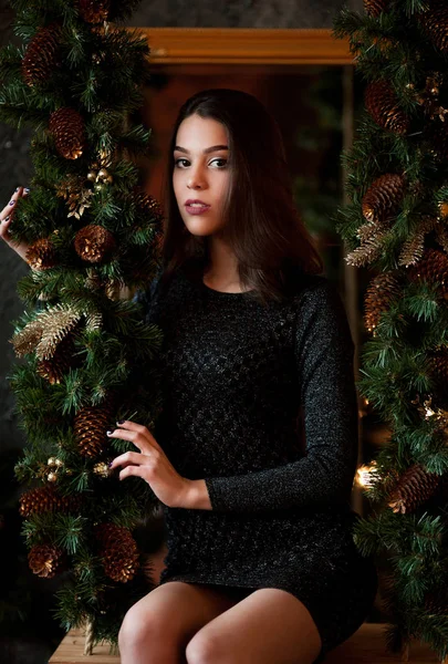 Portret siedzący dziewczyna w czarnej sukni w pobliżu Boże Narodzenie wieniec — Zdjęcie stockowe