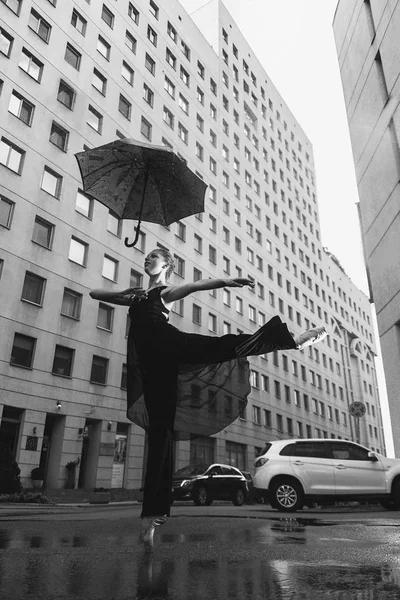 Ballerina with umbrella on city street under water drops