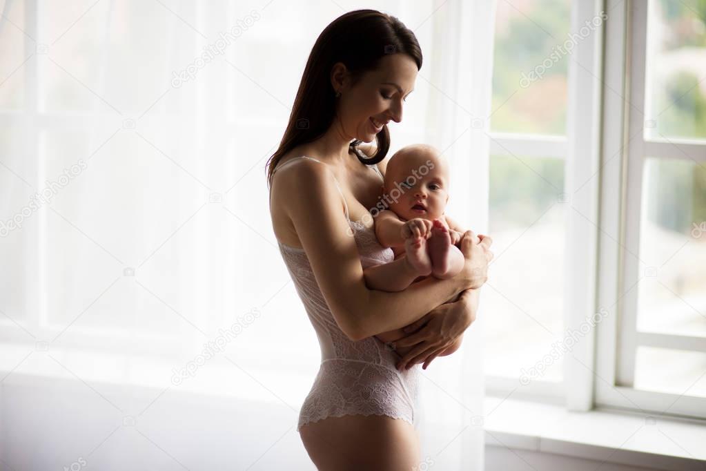 Young mother holding a naked baby on hands.