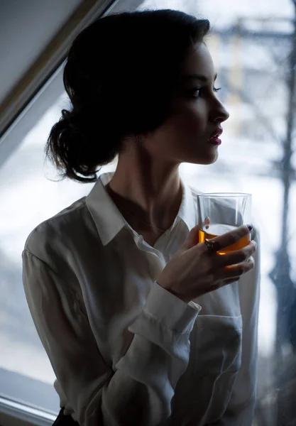 Mujer joven con vaso de whisky en el fondo de la ventana . — Foto de Stock