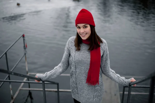 Menina de chapéu vermelho e cachecol andando no parque de inverno perto do lago . — Fotografia de Stock