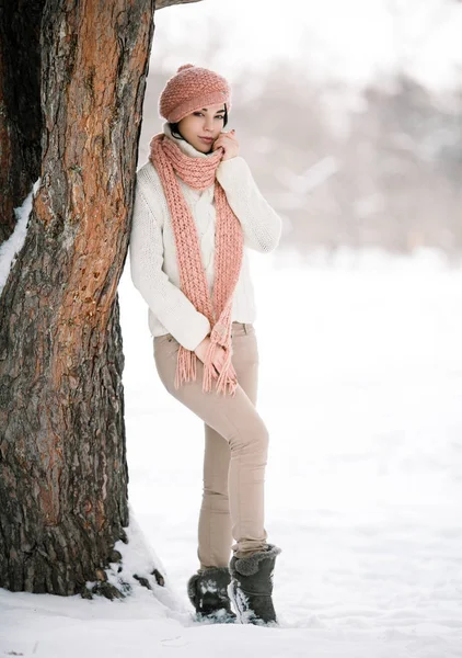 Flicka i tröja mössa och halsduk nära träd i vinter skog — Stockfoto