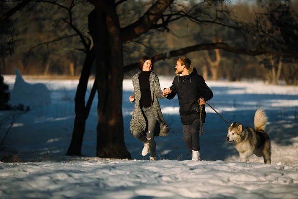 Chica y chico corriendo en el bosque de invierno con perro malamute . — Foto de Stock