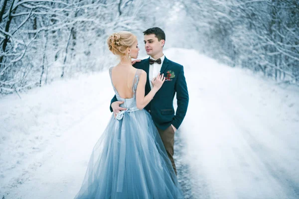 Bride and groom among snowy road in forest. — Stock Photo, Image