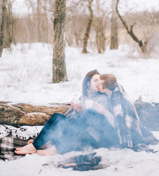 Junge Frau und Mann vor rauchendem Lagerfeuer im Winter — Stockfoto