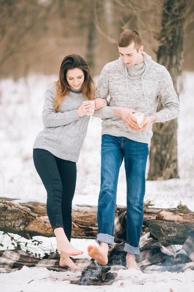 Jeune femme et homme réchauffe pieds nus sur le feu au pique-nique d'hiver . — Photo