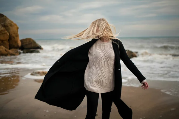 Woman in sweater and coat on winter beach in wind.