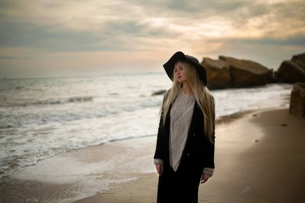 Vrouw in hoed en jas aan winter strand bij zonsondergang. — Stockfoto