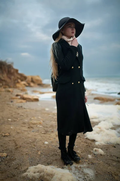 Donna in cappello e cappotto sulla spiaggia invernale tra schiuma di mare . — Foto Stock