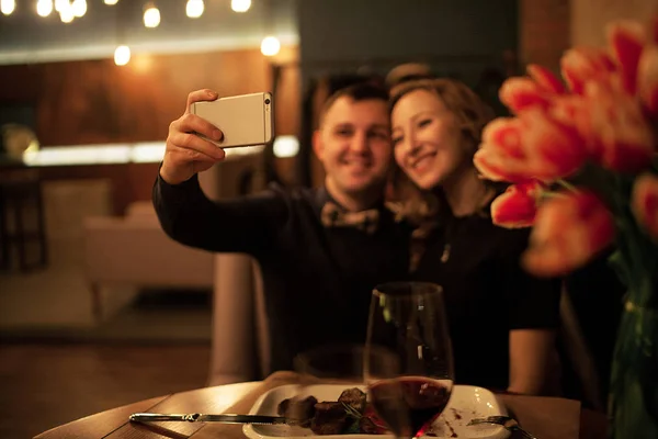 Joven hombre y mujer haciendo selfies por smartphone en restaurante . — Foto de Stock