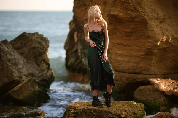 Jonge vrouw in groene jurk op strand onder de gele stenen en zee. — Stockfoto