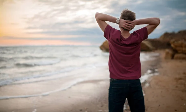 Jonge man in tee-shirt op winter strand bij zonsondergang. Achteraanzicht. — Stockfoto