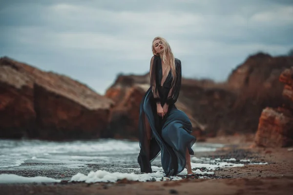 Jonge vrouw in lange transparante zwarte jurk bij strand en zee. — Stockfoto