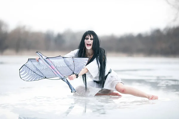 Onun elinde uçurtma ile buz göl kenarında oturan çılgın genç kadın. — Stok fotoğraf