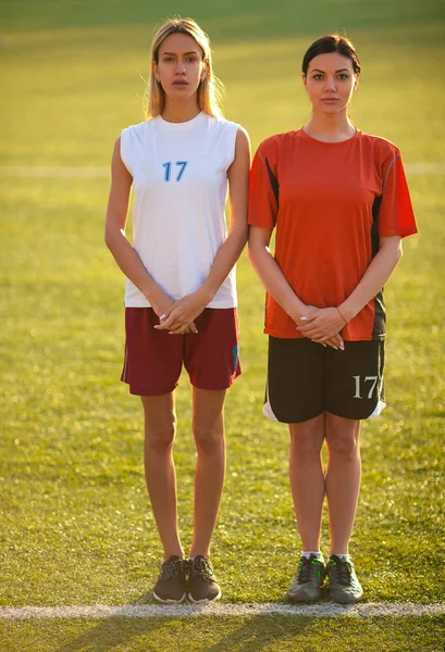 Two girls in a football uniform, stand on a football field waiti