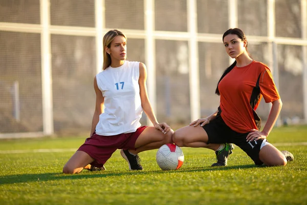 Two girls in a football uniform, sitting on a football field wit — Stock Photo, Image