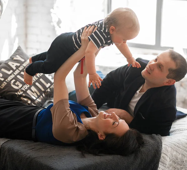 Unga föräldrar med små barn ligga på sängen och slänga det upp. — Stockfoto