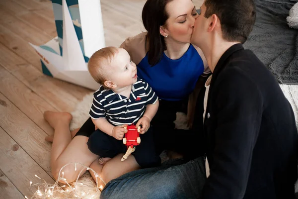 Jovens pais estão sentados no chão de madeira e beijando, bebê é i — Fotografia de Stock