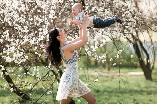 Ung mamma leker med hennes barn på promenad i blommande trädgård. — Stockfoto