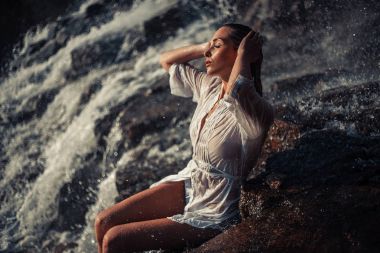 Beyaz gömlek ve bikini genç kadın rock yakınındaki waterfal oturur