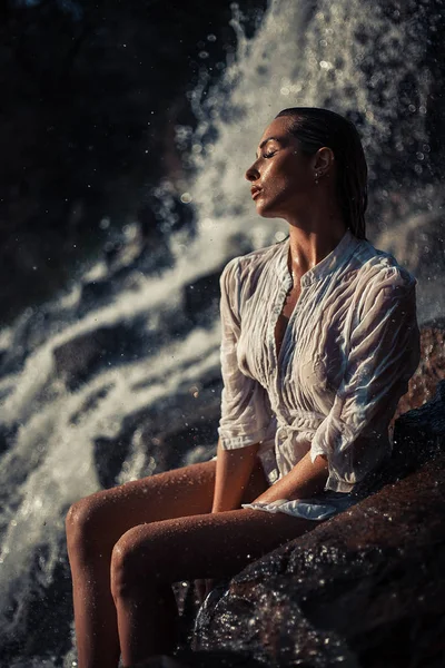 Jeune femme en chemise blanche et bikini assis sur le rocher près de Waterfal — Photo